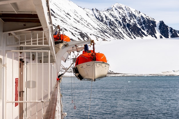 Lowering orange lifeboat to water in Arctic waters