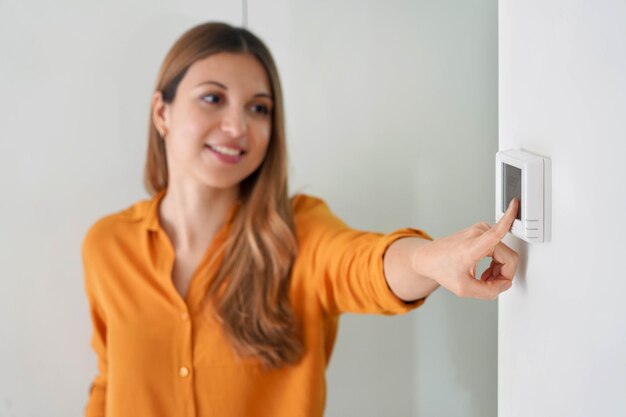 Foto abbassamento della temperatura per il risparmio energetico giovane donna che regola il termostato digitale del riscaldamento centralizzato a casa focus sulla mano