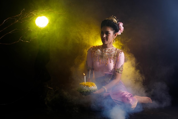 Loykrathong Dress of Thai Traditional Costume or South East Asia gold Dress in Asian Woman with decoration stand express feeling happy smile for Loy Krathong Floating festival over black background