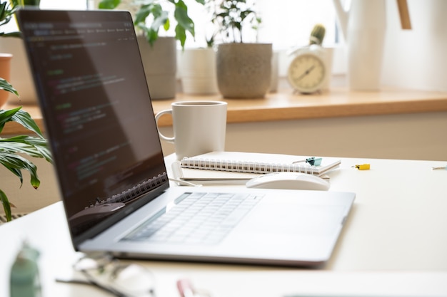 LThe laptop on a white desk in a bright office the code on the screen