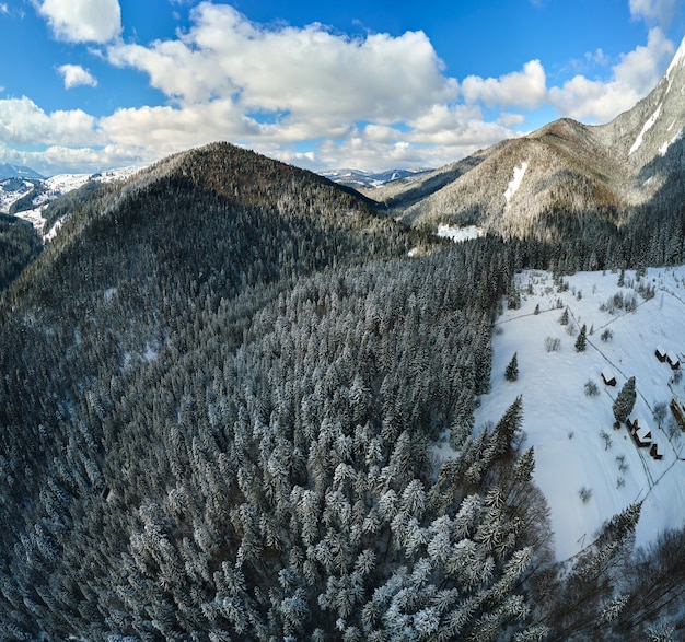 Lucht winterlandschap met kleine landelijke huizen tussen besneeuwde bossen in koude bergen.