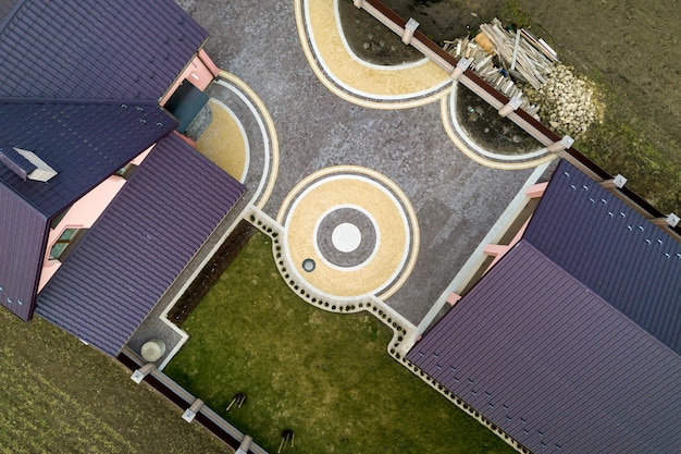 Luchtfoto bovenaanzicht van huis dakspaan dak op achtergrond van groen gazon en kleurrijke verharde tuin met geometrisch abstract patroon. Dak-, reparatie- en renovatiewerkzaamheden.