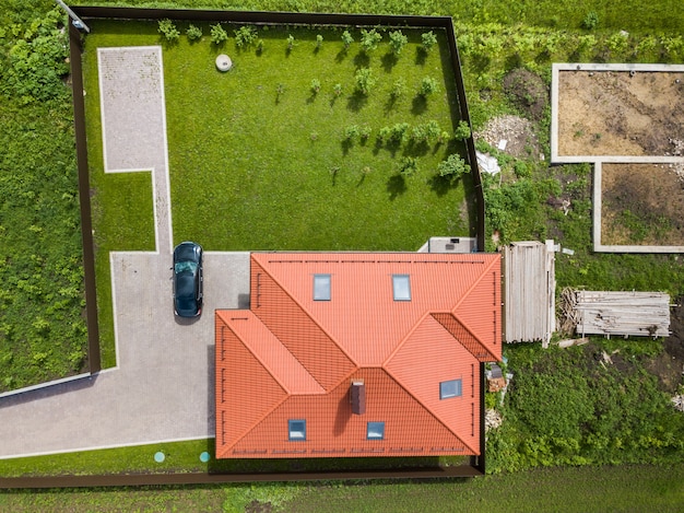 Luchtfoto bovenaanzicht van huis schindeldak met zolderramen en zwarte auto op verharde tuin met groen gazon.