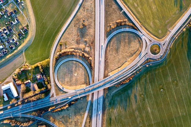 Luchtfoto bovenaanzicht van moderne snelweg weg kruising, huis daken op lente groen veld achtergrond. drone fotografie.