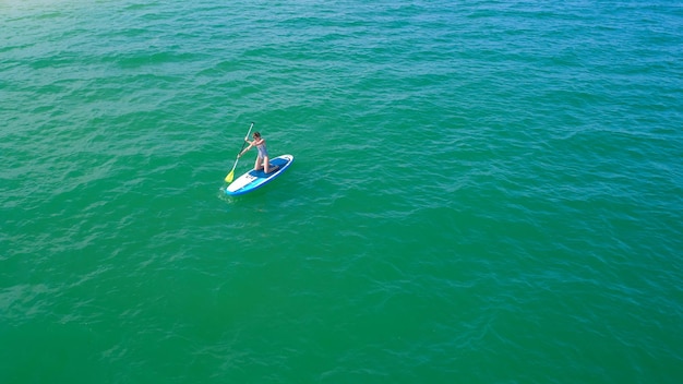 Luchtfoto drone vogelperspectief van jonge vrouw die sup board uitoefent in turquoise tropische heldere wateren