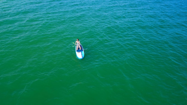 Luchtfoto drone vogelperspectief van jonge vrouw die sup board uitoefent in turquoise tropische heldere wateren