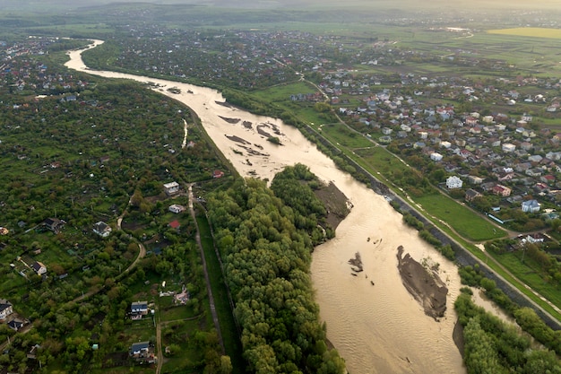 Luchtfoto landschap van kleine stad of dorp met rijen van residentiële huizen en groene bomen en grote flloded rivier.