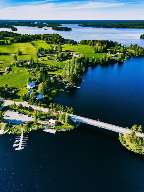 Luchtfoto mooie zomerse landschap met blauwe meer groene velden stadje met houten huizen en vissersboten aan de oever van water Plattelandsweg met brug in Finland