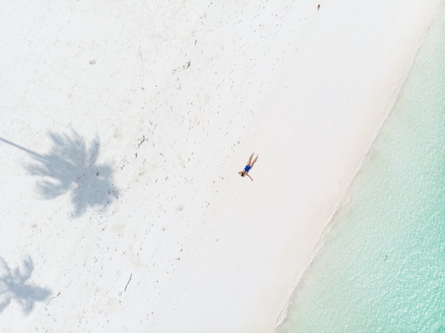 Luchtfoto top down weergave tropisch strand Caribische zee. Vrouw die tussen palmschaduw zonnebaadt op het witte turkooise water van het zandstrand