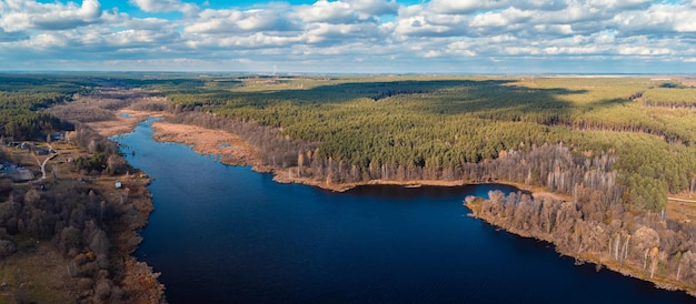 Luchtfoto uitzicht over het meer in de buurt van dennenbos en klein dorpje. Herfstfoto van een meer met schoon water dat de lucht weerspiegelt