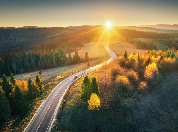 Luchtfoto van bergweg in bos bij zonsondergang in de herfst Bovenaanzicht van drone van weg in bos prachtig landschap met rijbaan in heuvels pijnbomen groene weiden gouden zonlicht in herfst reizen