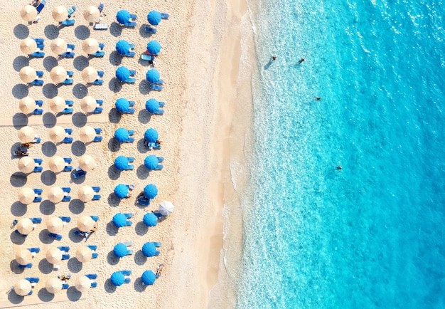 Luchtfoto van blauwe zee zandstrand met ligbedden en parasols bij zonsondergang in de zomer Tropisch landschap met turkoois water mensen ligstoel Reizen en vakantie Lefkada eiland Griekenland Bovenaanzicht