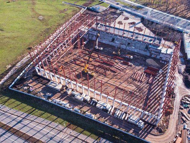 Luchtfoto van bouwplaats met metalen frame en vrachtwagenkranen.