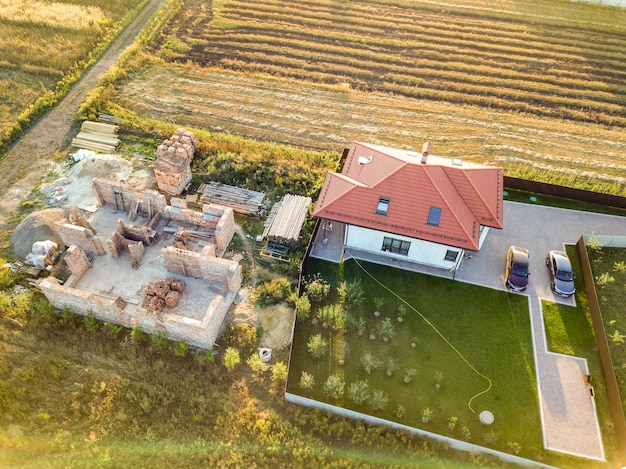 Luchtfoto van bovenaf van twee particuliere huizen, een in aanbouw met betonnen fundering en bakstenen muren en een ander afgewerkt met rood pannendak