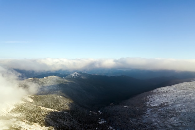 Luchtfoto van bovenaf van witte gezwollen wolken die besneeuwde bergtoppen bedekken in heldere zonnige dag.