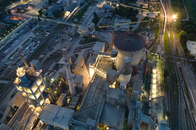 Luchtfoto van cementfabriek met hoge betonnen fabrieksstructuur en torenkranen op industrieel productiegebied 's nachts. Vervaardiging en wereldwijd industrieconcept.