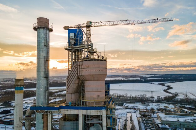 Luchtfoto van cementfabriek met hoge fabrieksstructuur en torenkraan op industrieel productiegebied bij zonsondergang.