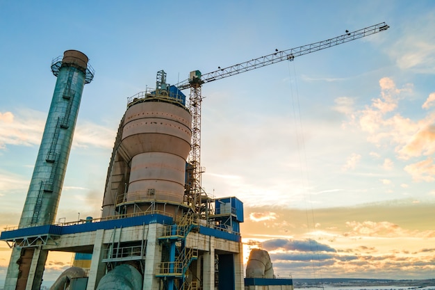 Luchtfoto van cementfabriek met hoge fabrieksstructuur en torenkraan op industrieel productiegebied bij zonsondergang.