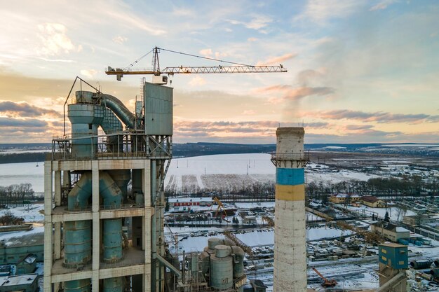 Luchtfoto van cementfabriek met hoge fabrieksstructuur en torenkraan op industrieel productiegebied bij zonsondergang.