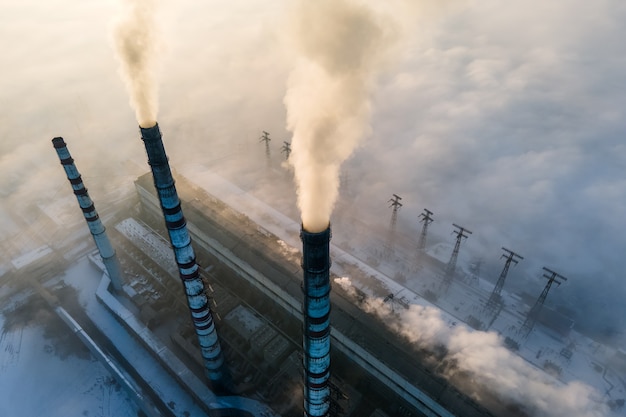 Luchtfoto van de hoge pijpen van de kolencentrale met zwarte rook die de vervuilende atmosfeer omhoog beweegt bij zonsondergang.