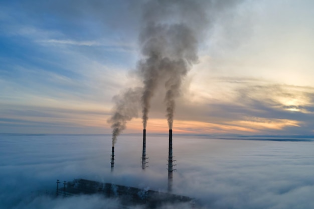 Luchtfoto van de hoge pijpen van de kolencentrale met zwarte rook die de vervuilende atmosfeer omhoog beweegt bij zonsondergang.