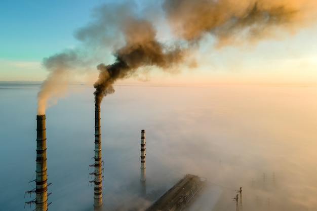 Luchtfoto van de hoge pijpen van de kolencentrale met zwarte rook die de vervuilende atmosfeer omhoog beweegt bij zonsopgang.