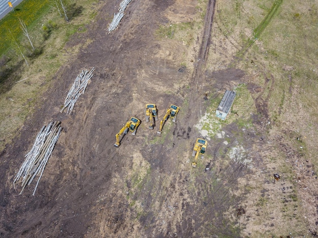 Luchtfoto van de vier gele rupsgraafmachines die bij de bouwplaats op de grond staan en wachten op het begin van de werkdag die de grond graaft in de buurt van omgevallen bomen en de weg