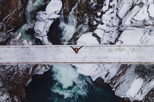 Luchtfoto van de vrouw die op de brug door de bergrivier staat.