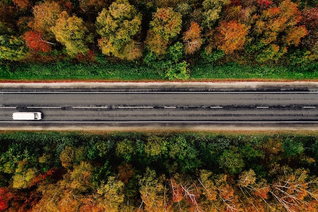 Luchtfoto van de weg en een auto in het herfstbos met rode gele en oranje bladeren Bovenaanzicht van bovenaf