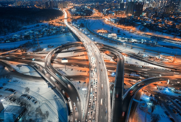 Luchtfoto van de weg in de moderne stad 's nachts in de winter. Bovenaanzicht van verkeer in snelweg, gebouwen, verlichting.