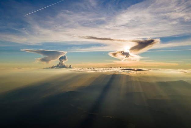 Luchtfoto van donkere bergheuvels met heldere zonnestralen van ondergaande zon bij zonsondergang Wazige pieken en mistige valleien in de avond