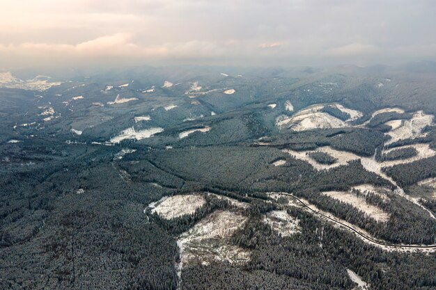 Luchtfoto van dorre winterlandschap met bergheuvels bedekt met groenblijvende dennenbos na zware sneeuwval op koude rustige avond.