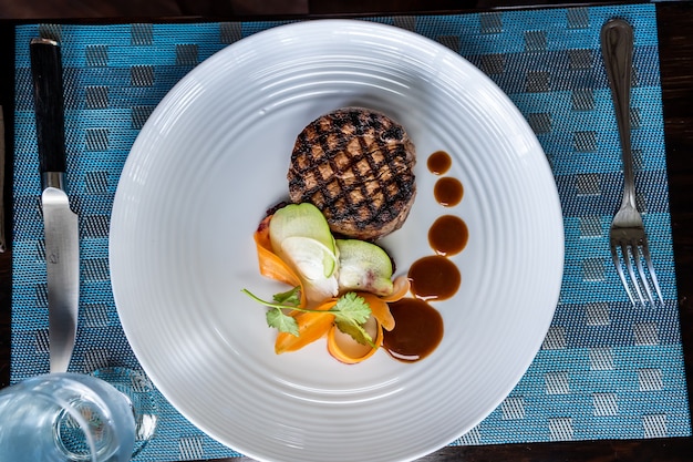 Luchtfoto van een gegrilde haasbiefstuk met groenten op een keramische plaat versierd met saus met vorken aan de zijkanten. Costa Ricaanse gastronomie