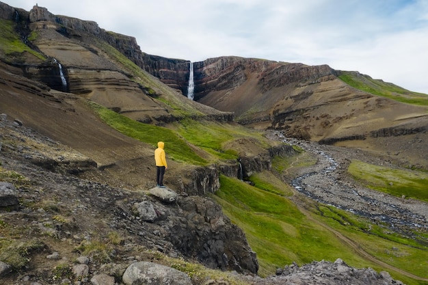 Luchtfoto van een man in een gele jas die geniet van de Hengifoss-waterval in IJsland