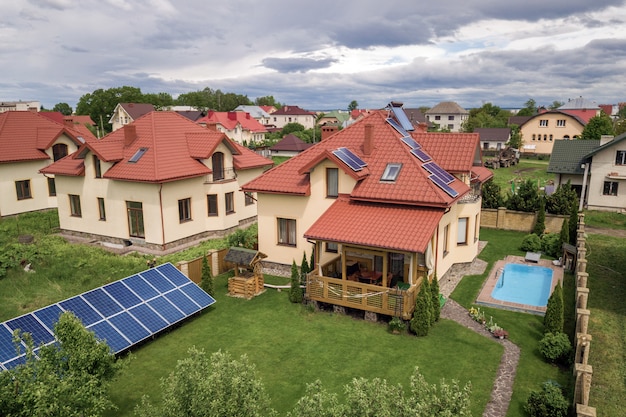 Luchtfoto van een nieuwe autonome woning met zonnepanelen en waterverwarmingsradiatoren op het dak en groene tuin met blauw zwembad.