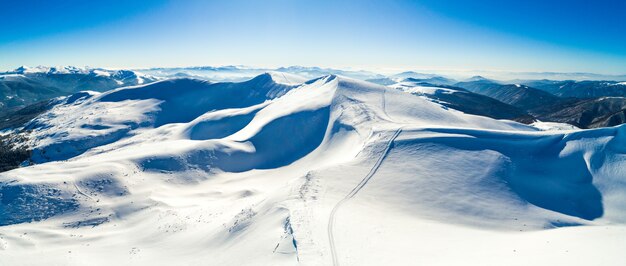 Luchtfoto van een prachtig besneeuwd skigebied met besneeuwde heuvels in de bergen en toeristische site op een zonnige heldere ochtend