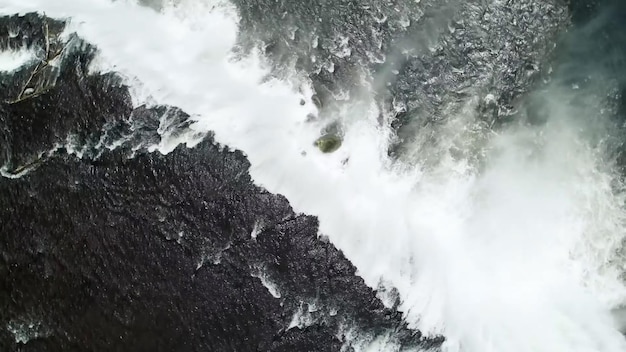 Luchtfoto van een surfer in een groen shirt op een rots in de oceaan.