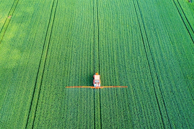 Luchtfoto van een tractor die landbouwvelden besproeit en herbiciden op het veld spuit