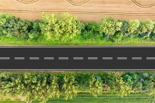 Luchtfoto van een weg tussen gele tarwevelden en groene bomen.