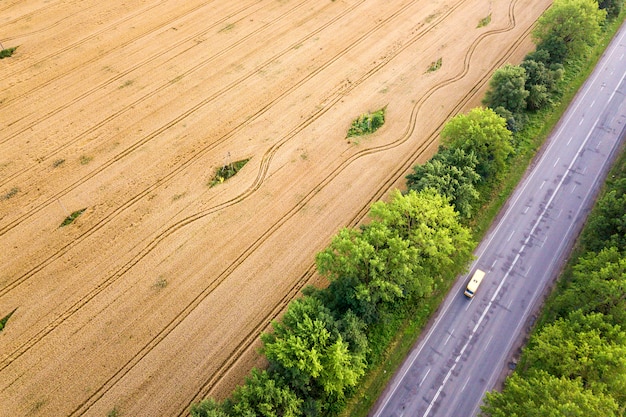 Luchtfoto van een weg tussen gele tarwevelden en groene bomen.