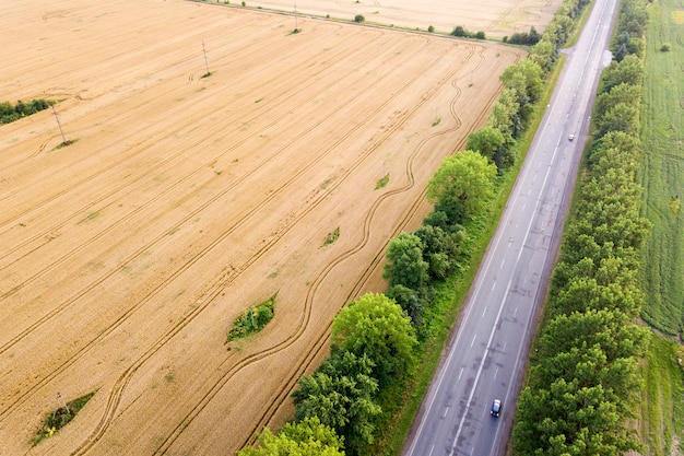 Luchtfoto van een weg tussen gele tarwevelden en groene bomen.