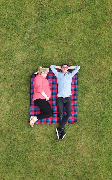 Luchtfoto van een zwangere vrouw en partner ontspannen in een park