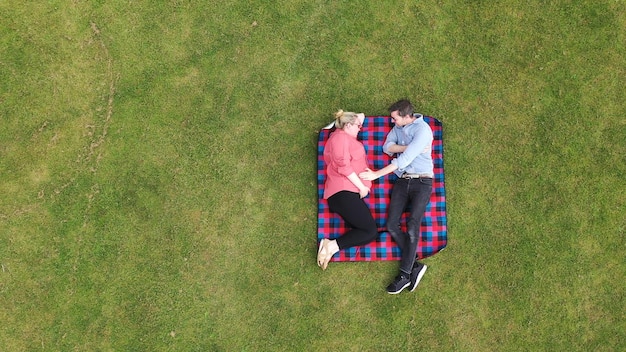 Luchtfoto van een zwangere vrouw en partner ontspannen in een park