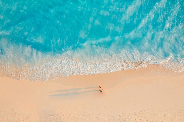 Luchtfoto van geweldig strand met paar wandelen in het licht van de zonsondergang dicht bij de turquoise zee. Bovenaanzicht