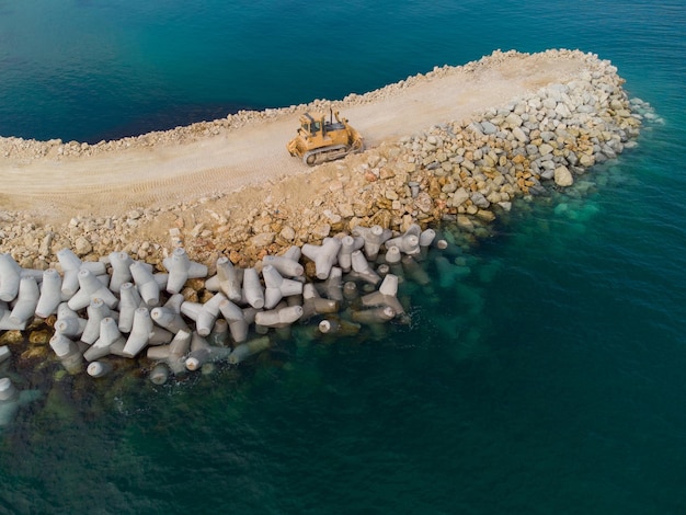 Foto luchtfoto van golfbrekerconstructie bulldozer op een stapel rotsblokken in de zee