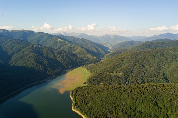 Luchtfoto van groot meer met helder blauw water tussen hoge bergheuvels bedekt met dicht groenblijvend bos.