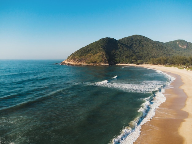 Luchtfoto van Grumari Beach, een paradijs aan de westkant van Rio de Janeiro, Brazilië. Grote heuvels rondom. Zonnige dag bij dageraad. Groenachtige zee. Drone foto.