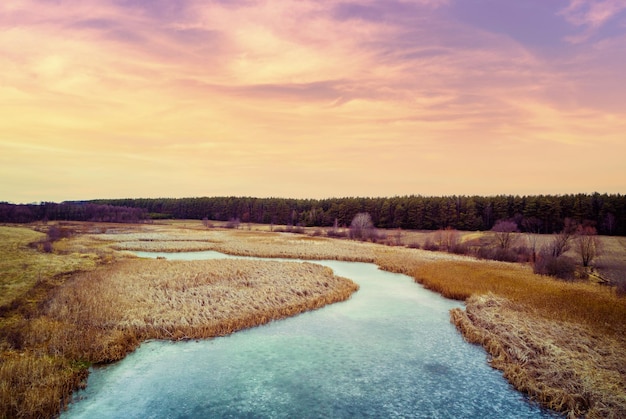 Luchtfoto van het landschap en de bevroren kronkelende beek in de avond bij zonsondergang