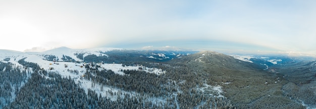 Luchtfoto van het prachtige winterpanorama van de besneeuwde hellingen en heuvels tussen de weelderige witte wolken