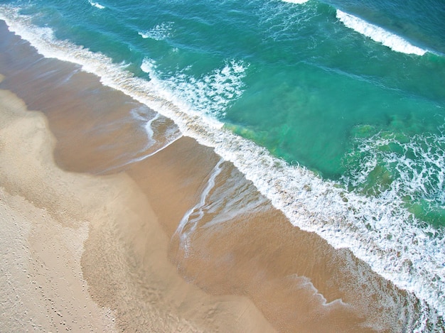 Luchtfoto van het schuim van de golven van de zee met oranje zand en groen water